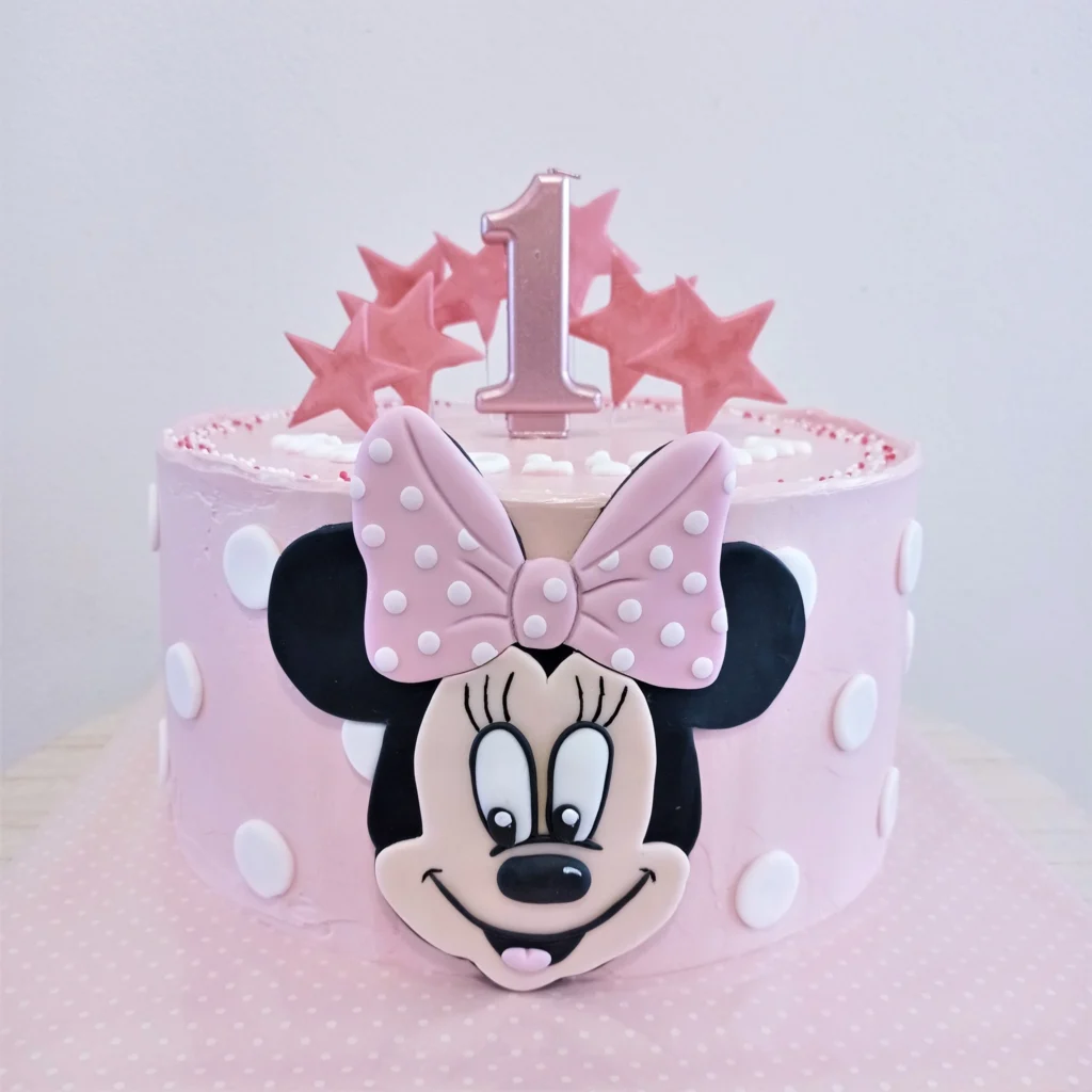 Růžový bezlepkový dort s obličejem Minnie Mouse, puntíky a hvězdičkami, k 1. narozeninám.